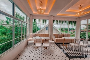 Una habitación con comedor, sofá y grandes ventanales con vistas a zonas verdes.