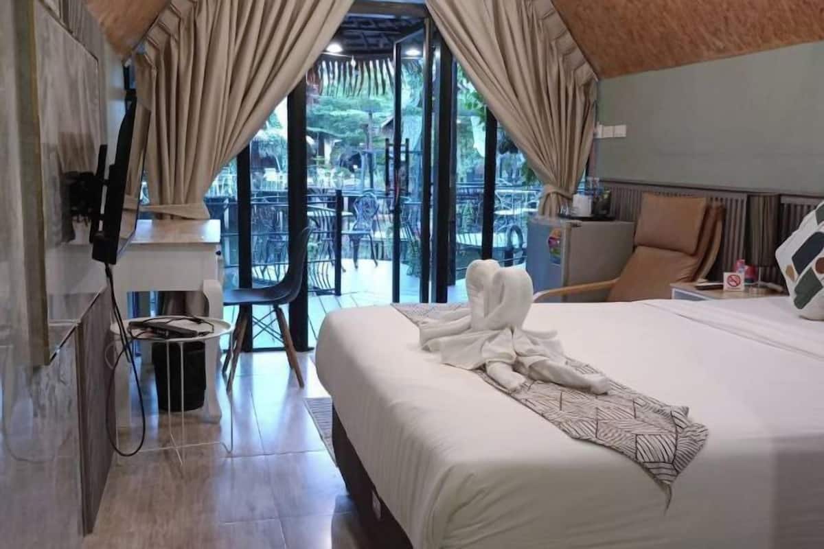 A hotel room with a large bed, a TV mounted on the wall, and a balcony with outdoor seating.
