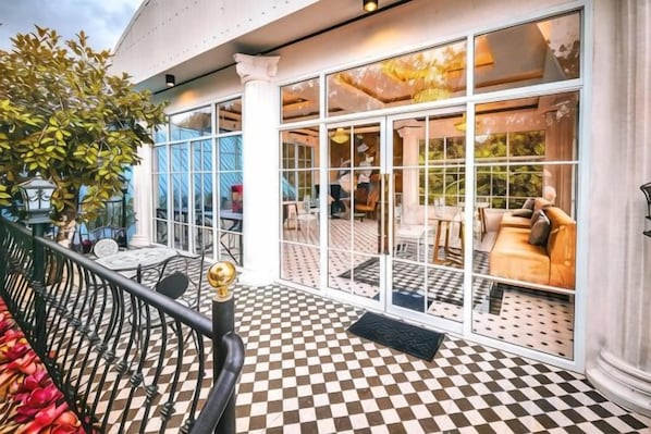 An outdoor seating area with tables and chairs, a checkered floor, and a view into the interior through large windows.