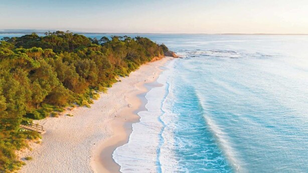 Une plage avec une promenade en bois, un rivage sablonneux et des vagues de l’océan.