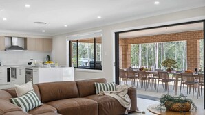 Une cuisine moderne avec des meubles blancs, un coin repas comprenant une table et des chaises, et une grande porte-fenêtre coulissante donnant sur un espace extérieur.