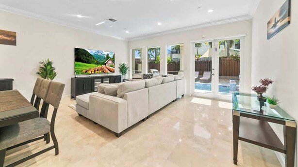 A spacious living room with a large sofa, a dining area with a table and chairs, a flat-screen TV, and a glass coffee table.