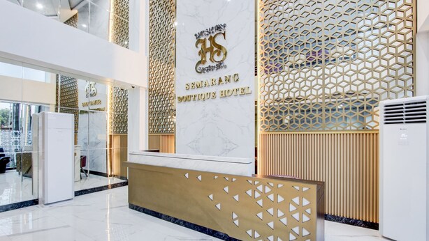 Un hall d’hôtel avec un comptoir de réception en marbre, un mur orné d’un motif géométrique et un logo placé au-dessus du comptoir de réception.