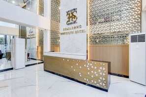 Zona de recepción de un hotel con un mostrador de mármol, una pared con diseño geométrico y un logotipo sobre el mostrador.
