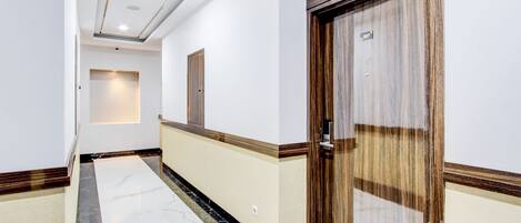 A hallway with a marble floor, wooden paneling, and a door with a number plate.