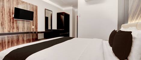 A modern hotel room with a large bed, a flat-screen TV mounted on a wooden wall, a mirror, and an air conditioning unit.