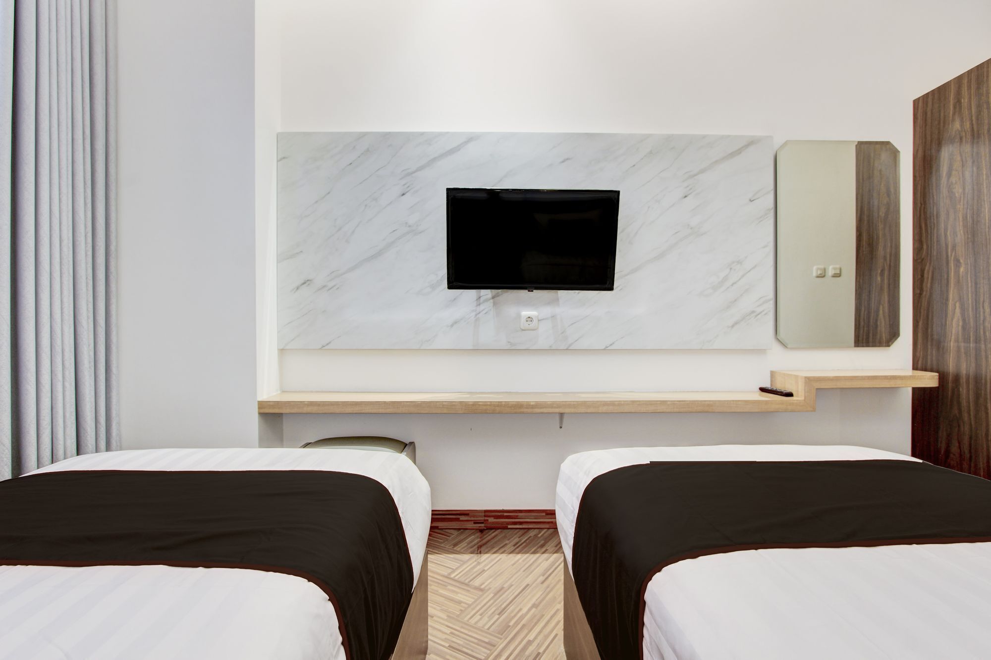 Une chambre d’hôtel avec deux lits, un téléviseur fixé au mur en marbre, une étagère en bois et un miroir.