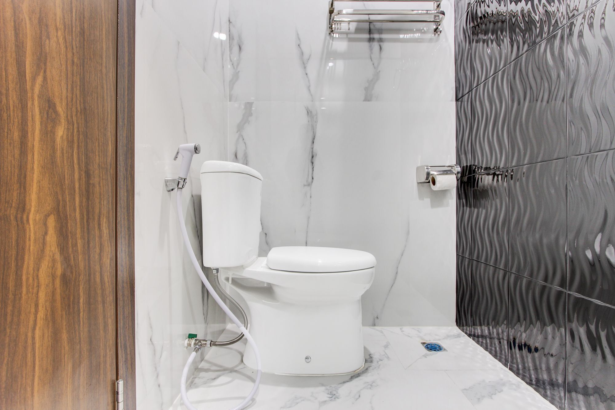 Un baño moderno con inodoro, paredes de mármol y zona de ducha.