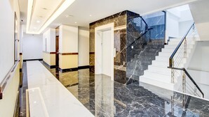 Un intérieur moderne avec un sol en marbre, un escalier et un couloir menant à une porte.