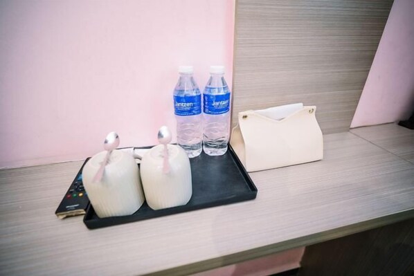 Habitación de hotel con una bandeja negra que sostiene dos almohadas blancas, un control remoto y dos botellas de agua sobre una superficie de madera.