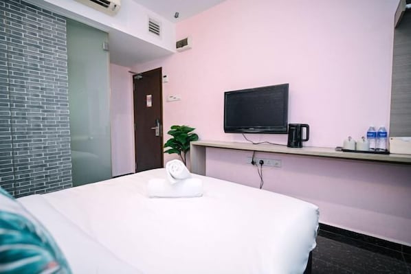 Hotellihuone, jossa on sänky, seinälle asennettu televisio, huonekasvi ja kahvinkeitin.