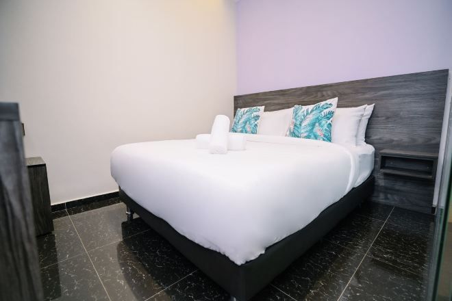 A neatly made bed with white linens, a dark headboard, and a pair of pillows with a leaf pattern.