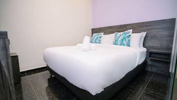 A neatly made bed with white linens, a dark headboard, and a pair of pillows with a leaf pattern.