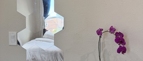 A wall-mounted mirror with a hexagonal design, a potted orchid, and a light switch.