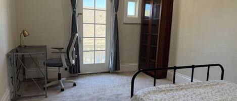 Un dormitorio con cama, un escritorio con silla, armario y ventana con cortinas.