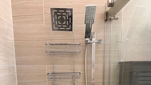 Un'area doccia con soffione a mano, pannello di controllo a parete e box doccia in vetro.