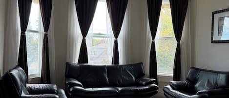 A modern living room with a black leather sofa set, a white coffee table, and a large window with curtains.