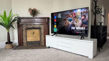 Una sala de estar con una televisión de pantalla plana sobre un mueble blanco, una chimenea y una planta en maceta.