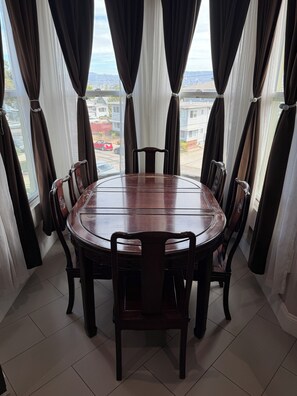 A dining area with a round table and chairs, large windows with curtains, and a view of a residential area. - Alameda Modern Victorian 4BD unit A (Alameda)