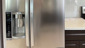 Ein Edelstahl-Kühlschrank mit integriertem Wasserspender und separatem Gefrierfach.