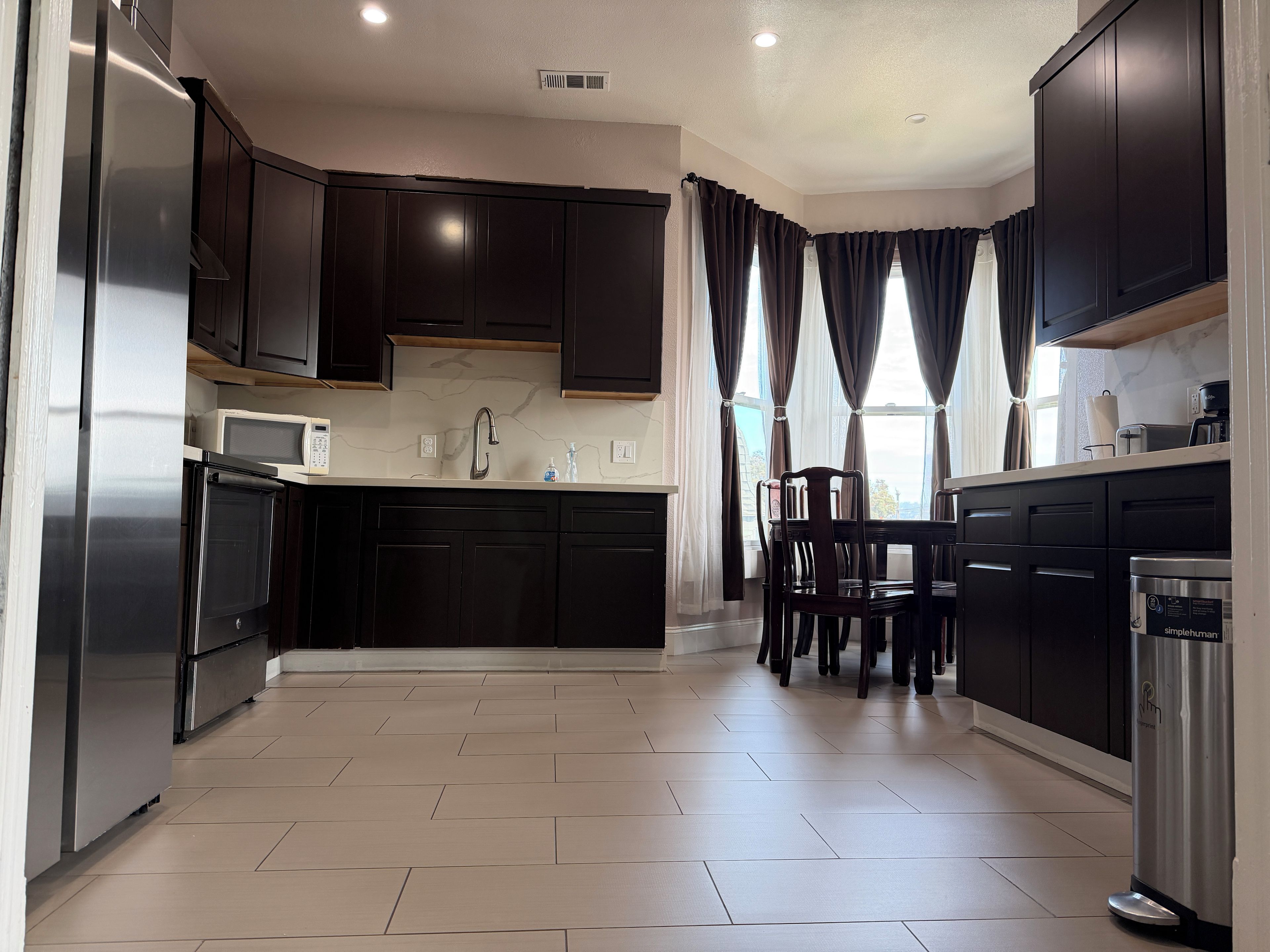 A modern kitchen with dark cabinetry, a stainless steel refrigerator, a microwave, and a coffee machine.