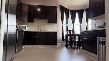 A modern kitchen with dark cabinetry, a stainless steel refrigerator, a microwave, and a coffee machine.