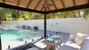 A poolside area with a covered seating area, a table with blue cups, and a lounge chair. - Byron Oakland Oasis (Byron Bay)