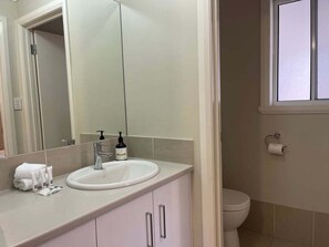 A bathroom with a white sink, a mirror, and a toilet. - Glen’s Everyday Stay - Outdoor Firepit (Wagga Wagga)
