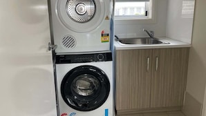 Un espace buanderie compact comprenant un lave-linge et un sèche-linge à chargement frontal, un évier et une fenêtre située au-dessus de l’évier.