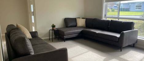 A living room with a sectional sofa, a small side table, and a window with a view of the outside.