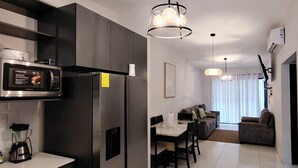 Une cuisine moderne équipée d’un four à micro-ondes, d’un réfrigérateur et d’une machine à café intégrés. On y trouve un coin repas avec une table et des chaises, ainsi qu’un canapé à l’arrière-plan.
