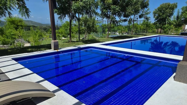 Une piscine rectangulaire aux carreaux bleus, entourée d’une terrasse en béton et d’un auvent incurvé servant de protection contre le soleil.