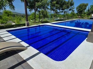 Una piscina rectangular con azulejos azules, rodeada por una plataforma de hormigón y un toldo curvo.