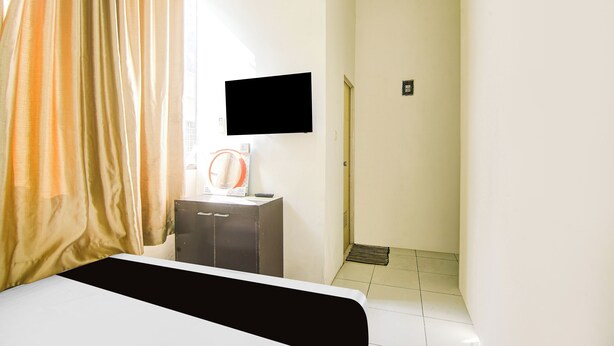 A hotel room with a bed, a TV mounted on the wall, a small cabinet, and a shower area. - Hotel O Makassar near RS Grestelina formerly Wisma Makassar (Makassar)