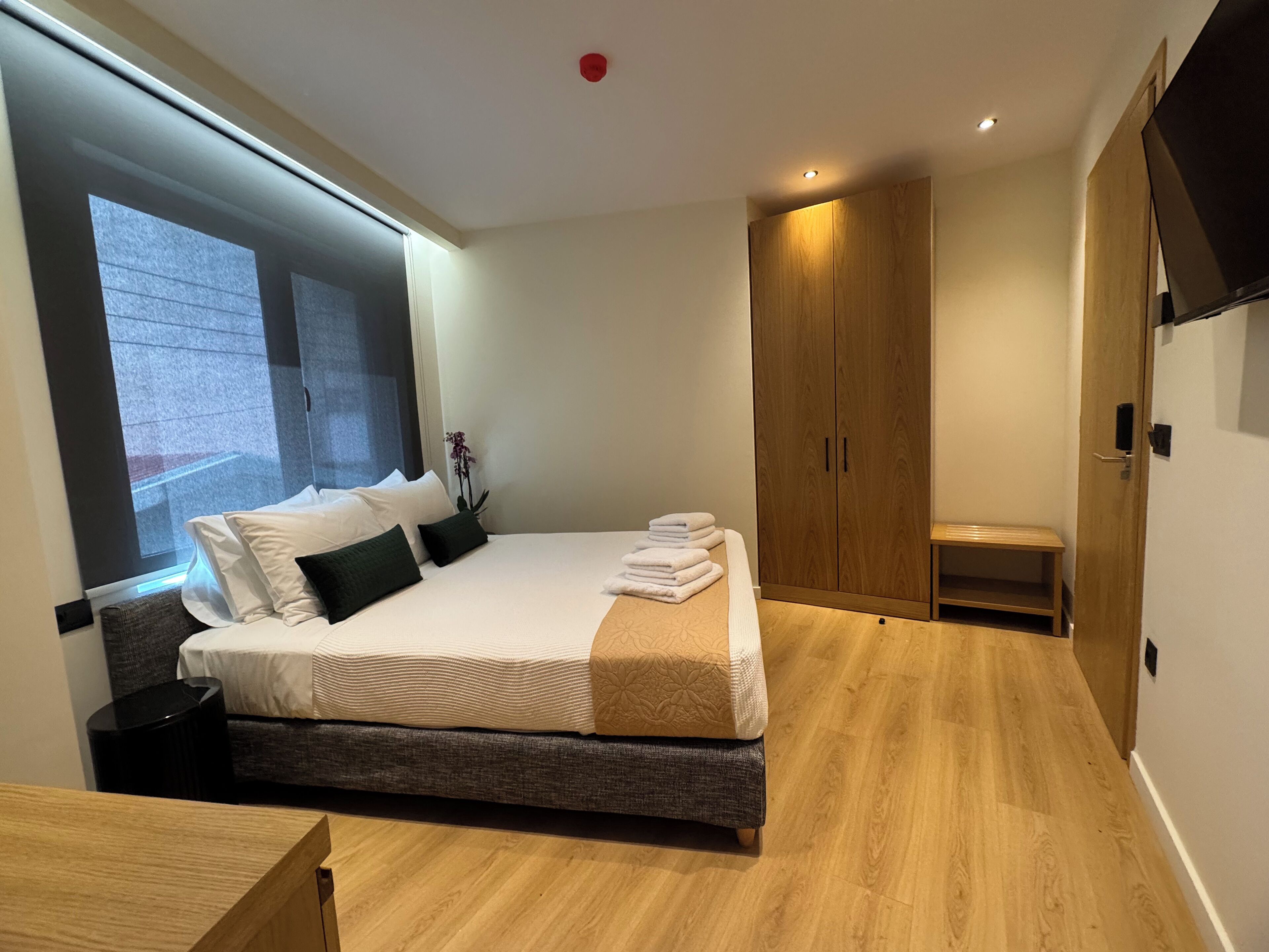 A modern bedroom with a large bed, wooden wardrobe, and a small seating area.