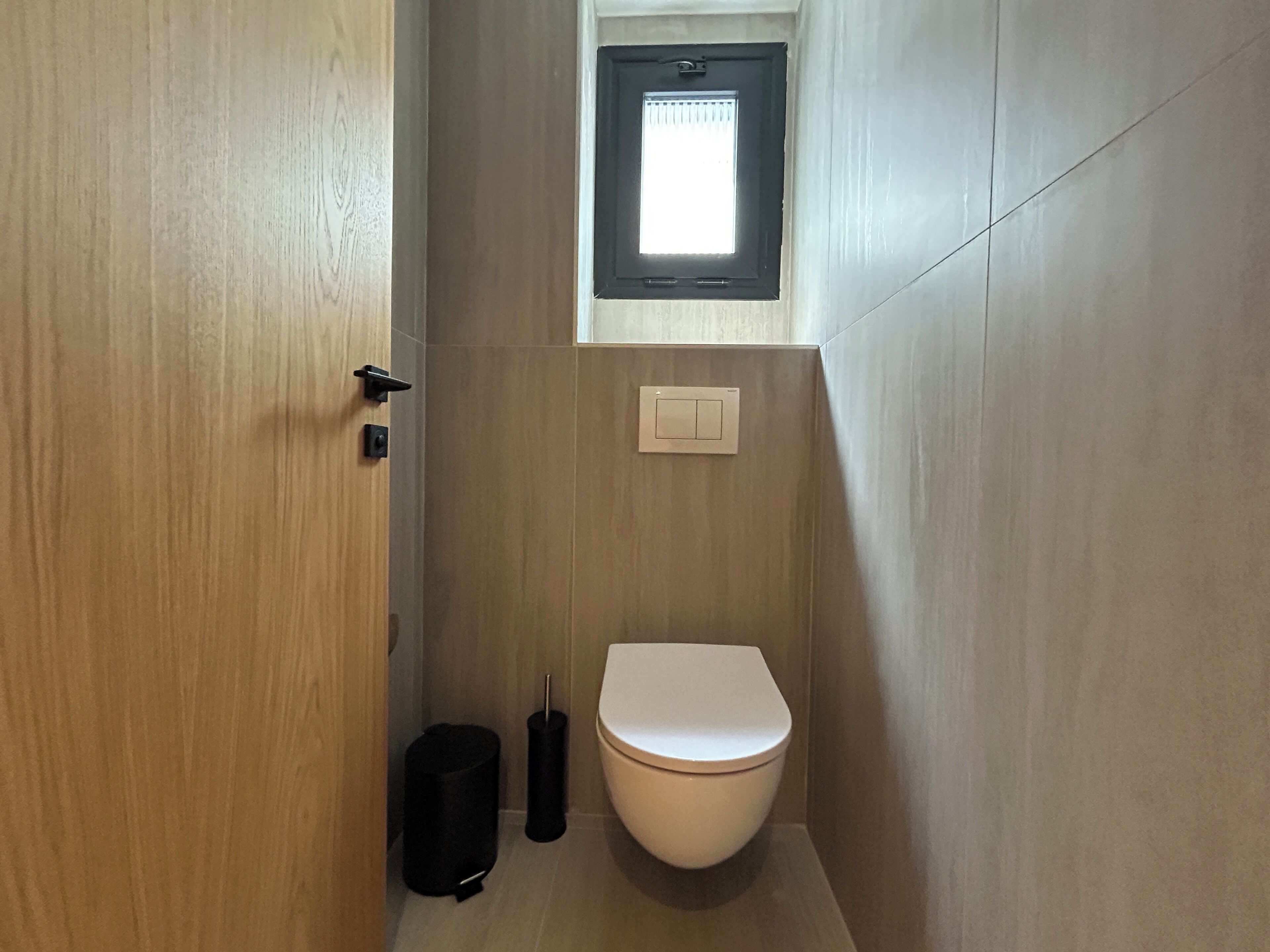 A compact bathroom with a toilet, a small window, and a light switch on the wall.