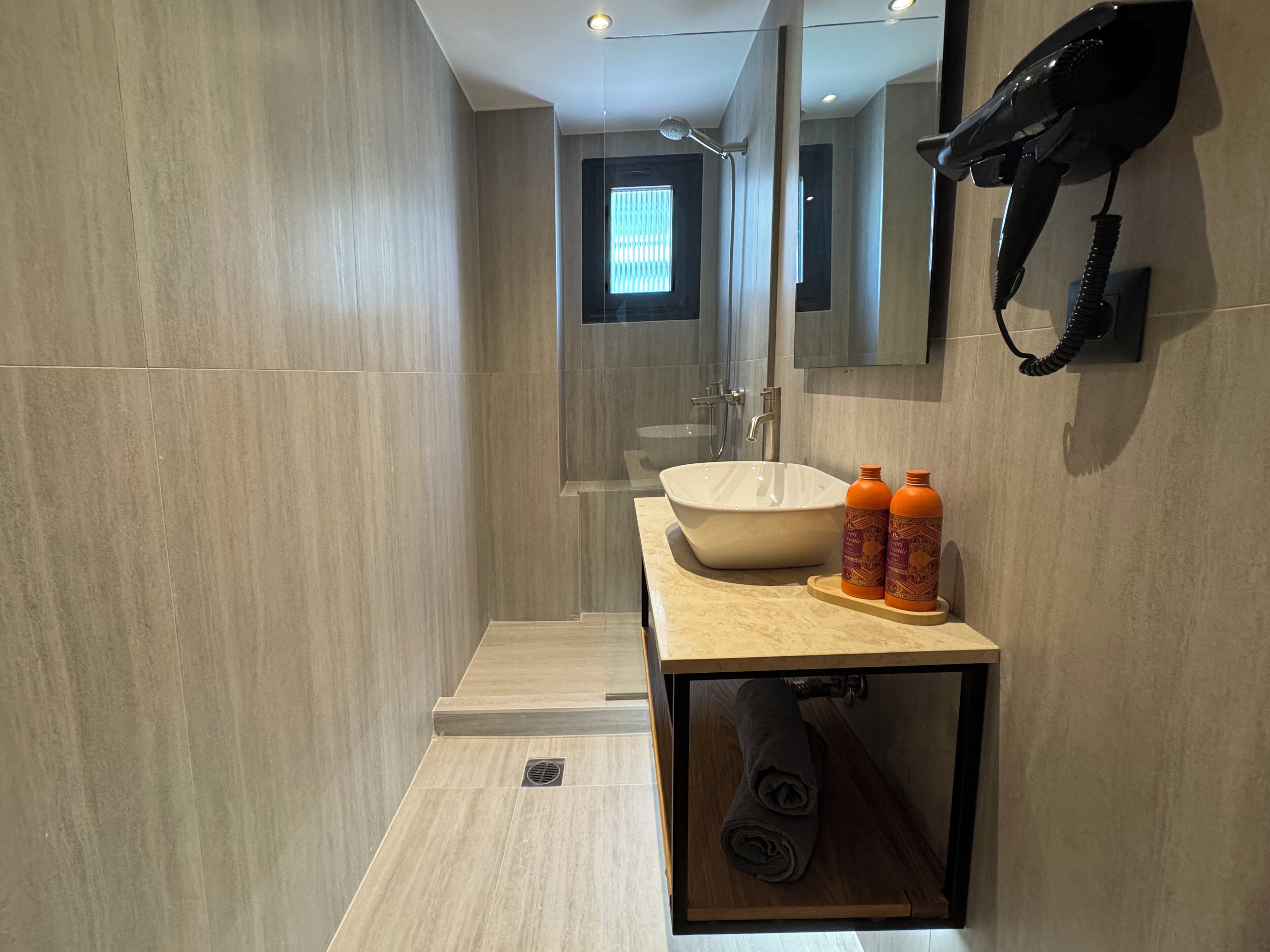 A modern bathroom with a large sink, a mirror, and a hairdryer mounted on the wall.