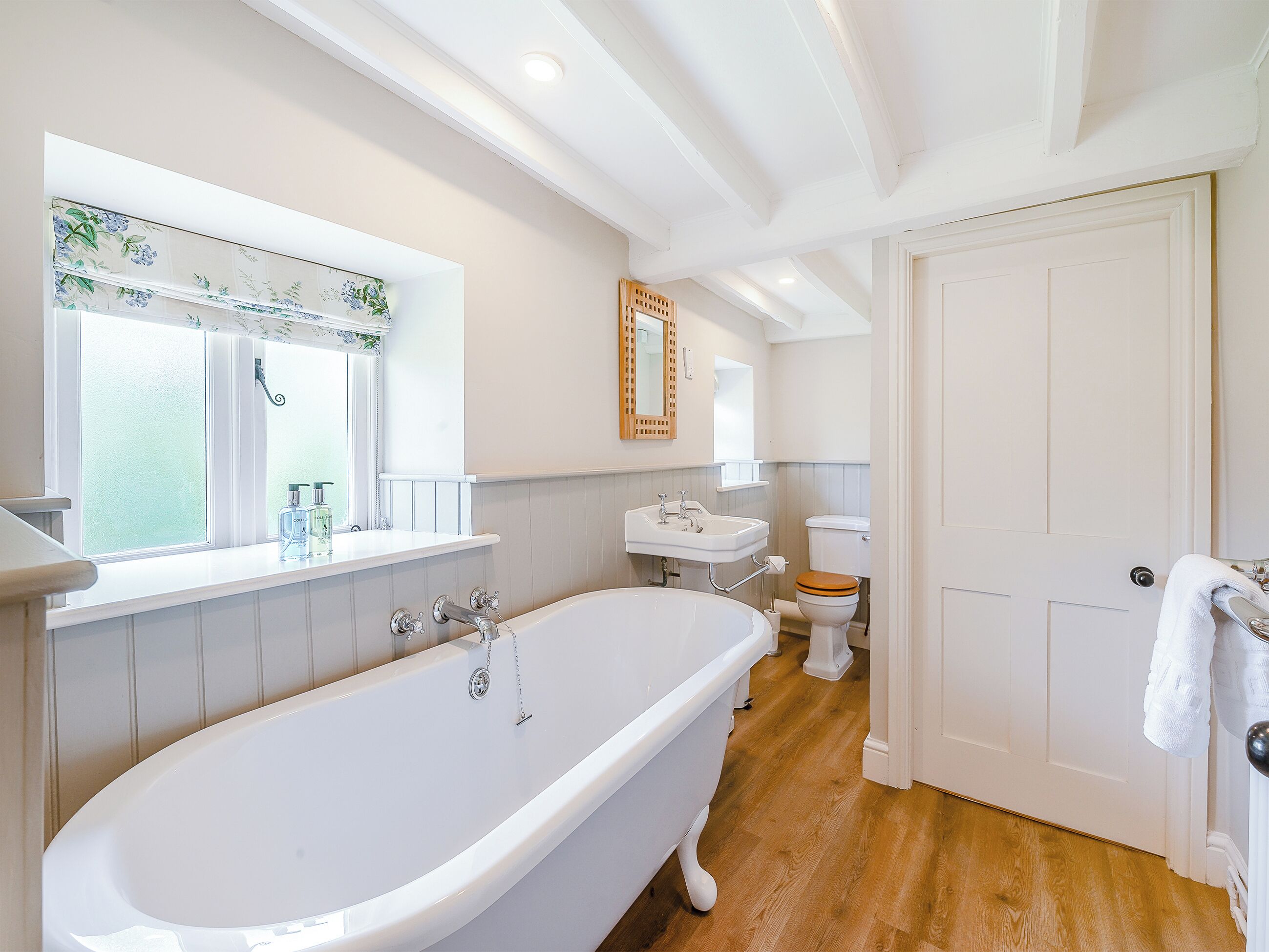 A bathroom with a freestanding bathtub, a toilet, a sink, and a window with a floral design.