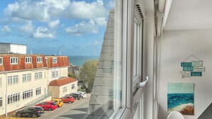 A view from a window overlooking a street with parked cars, a building with a red roof, and a sign with beach-related text. - 3 bedroom accommodation in Westbourne, near Bournemouth (Westbourne, near Bournemouth)