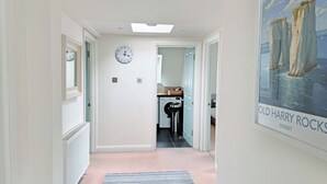 A hallway with a clock, a washing machine, and a poster of Old Harry Rocks. - 3 bedroom accommodation in Westbourne, near Bournemouth (Westbourne, near Bournemouth)