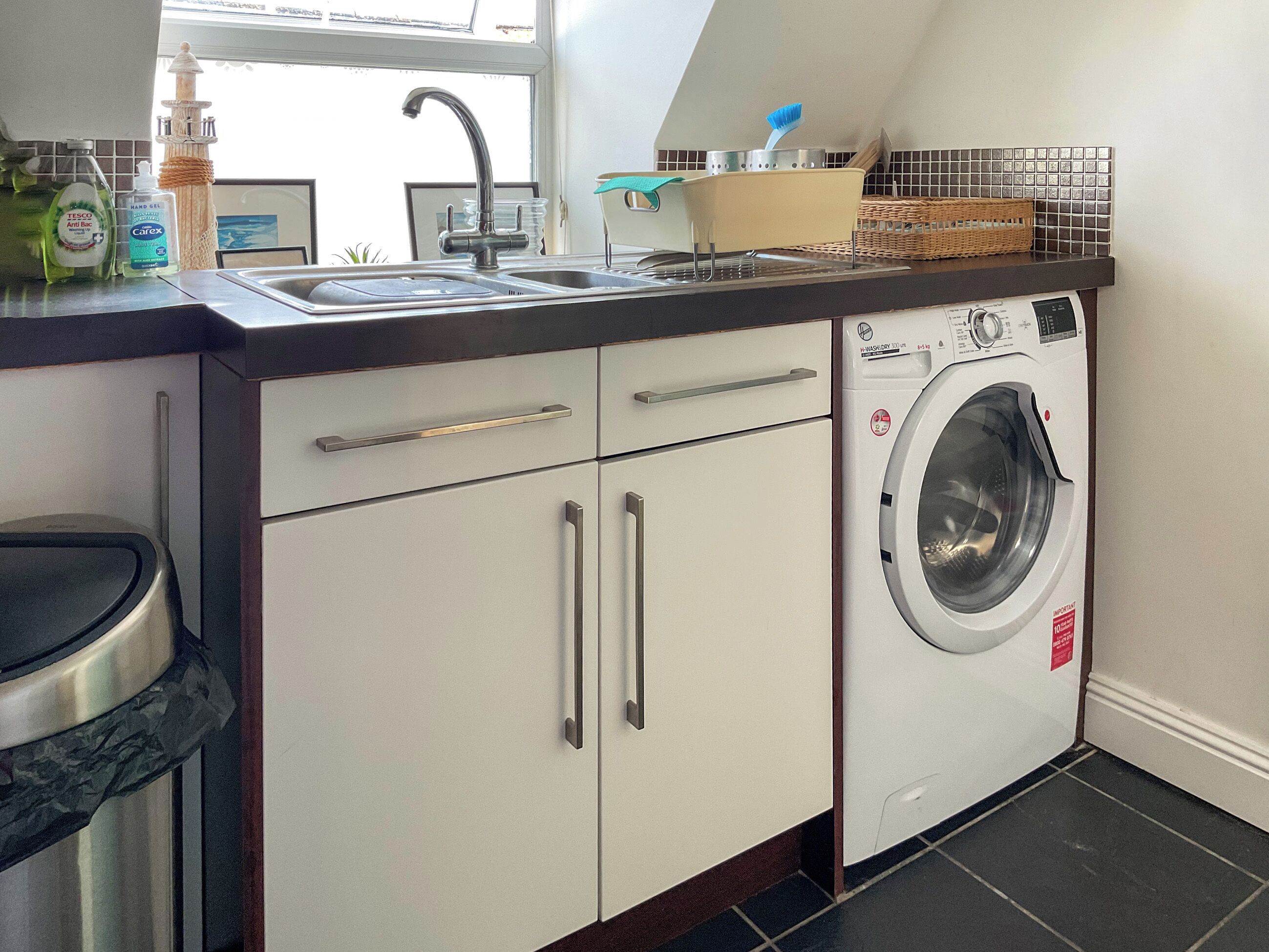 Een kleine keuken met een wasmachine, een spoelbak en diverse keukenbenodigdheden.