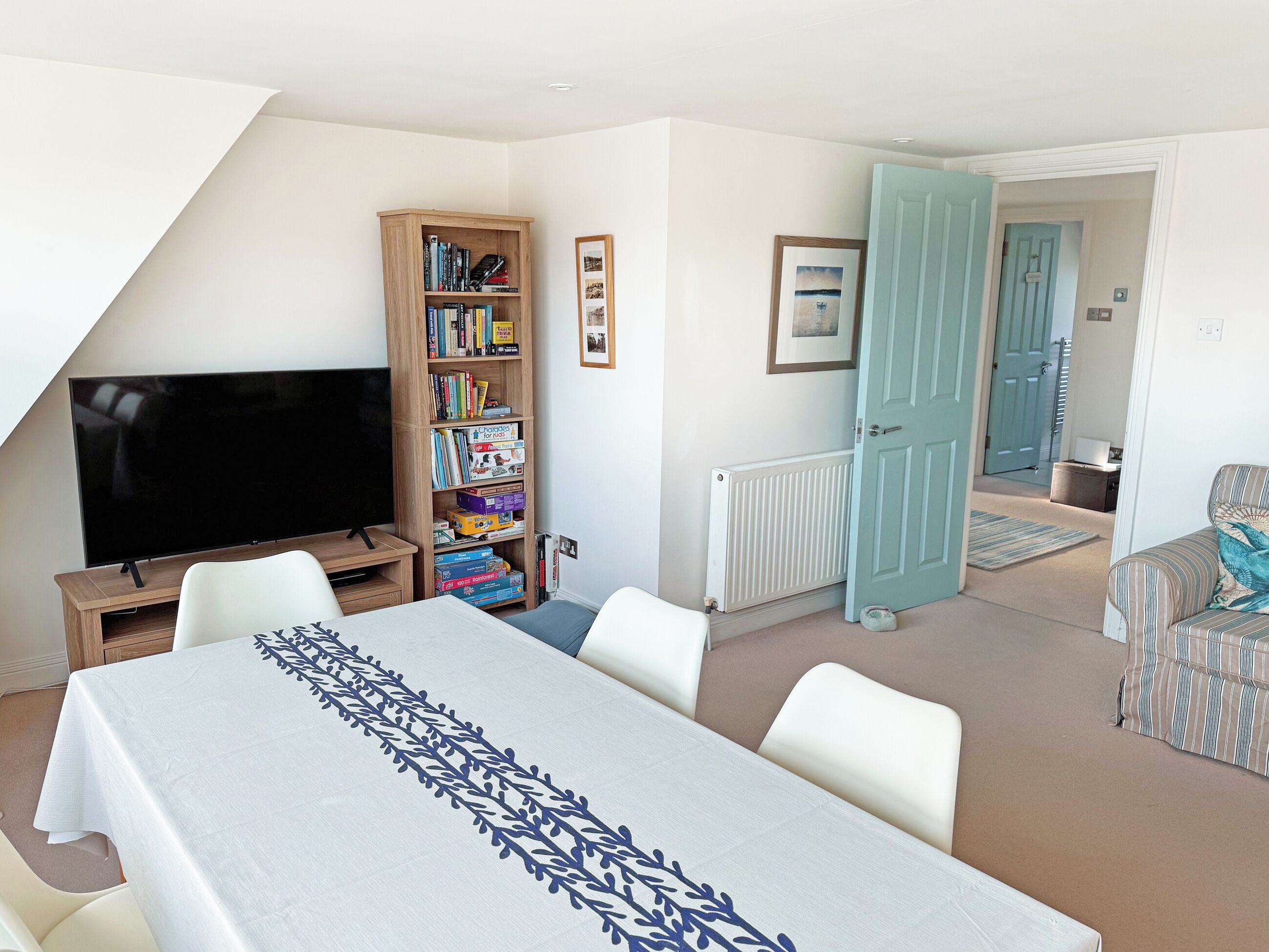 A room with a TV, bookshelf, dining table, and a door leading to another room.