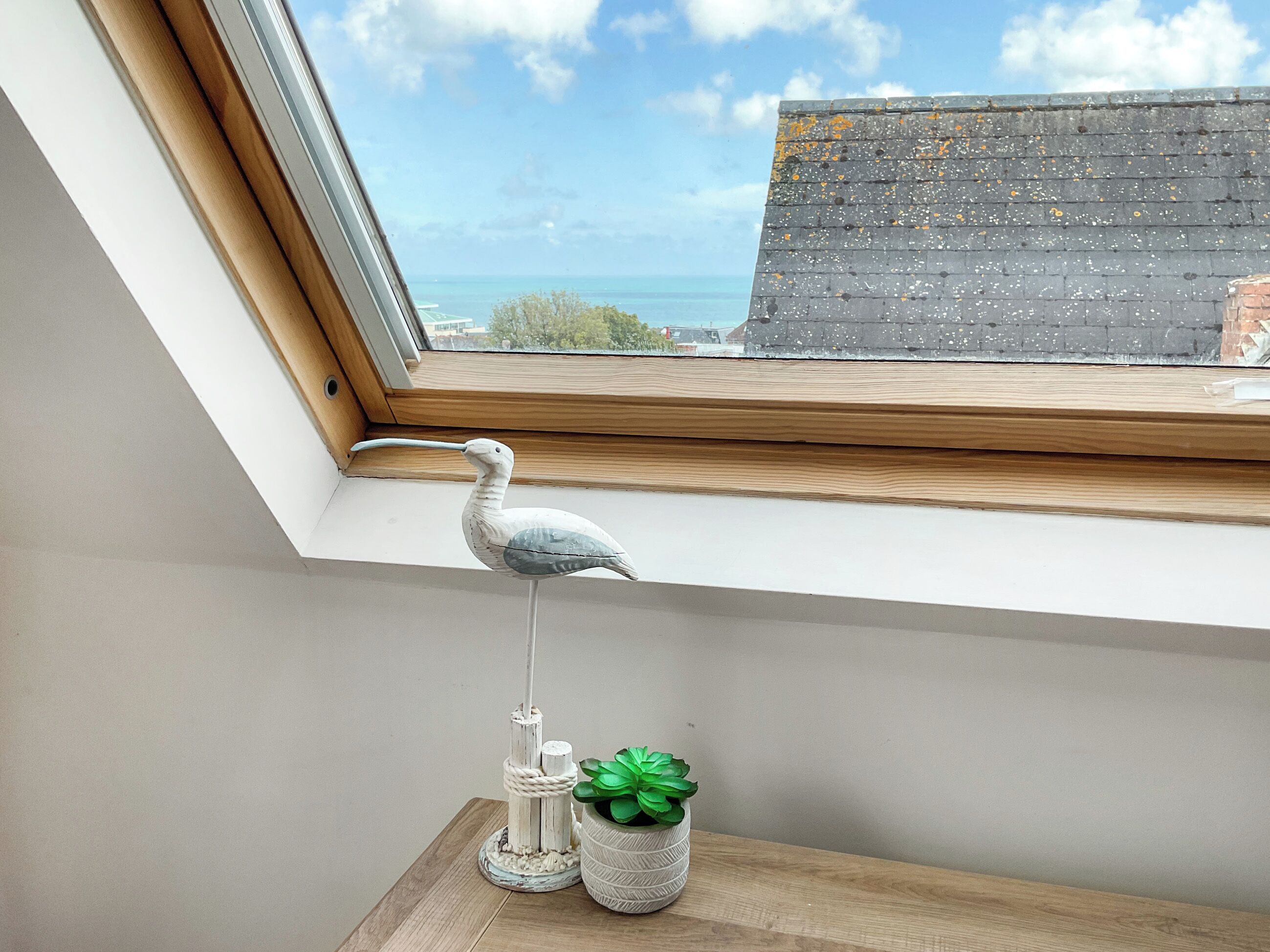 A skylight window with a decorative bird sculpture, a small plant, and a candle holder on a wooden shelf.