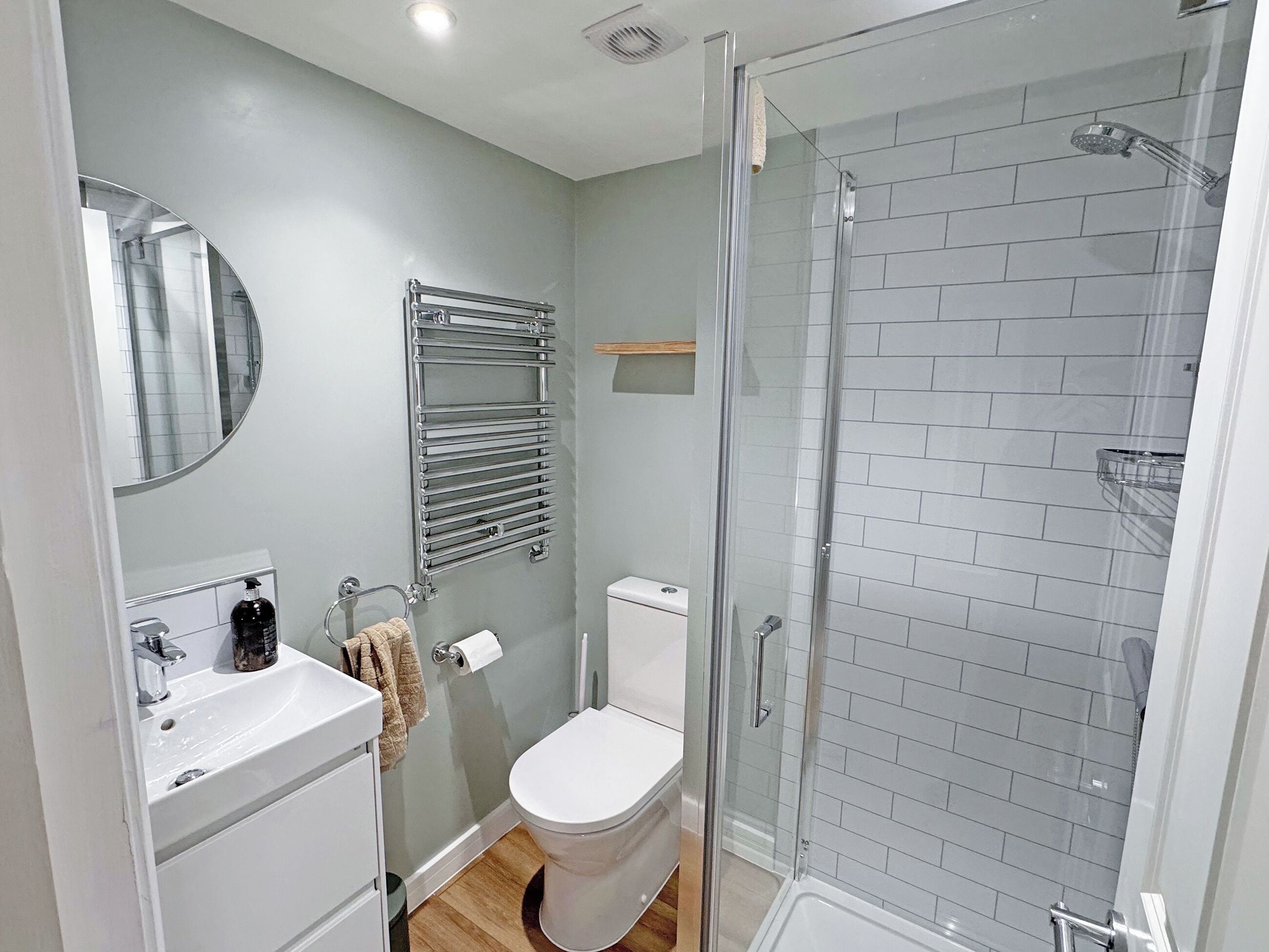 A bathroom with a toilet, sink, mirror, towel rack, shower, and glass door.