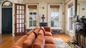 Ein großzügiger Raum mit einer großen Couch, einem Kamin und Blick auf die Straße durch mehrere Fenster.