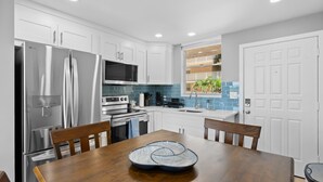 A modern kitchen with white cabinets, stainless steel appliances, and a wooden dining table.