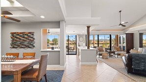 A spacious living area with a dining table, chairs, a sofa, and a large window offering a view of the outdoors.