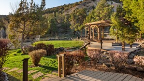 Un terrazzo in legno con una pergola, una zona verdeggiante e montagne sullo sfondo.