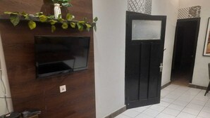 Een kamer met een flatscreen televisie aan een houten wand, een zwarte deur en een betegelde vloer.