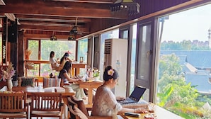 A wooden interior with large windows, wooden furniture, and a view of greenery and buildings outside. - Zhaizili Resort Xishuangbanna  (Xishuangbanna Dai)